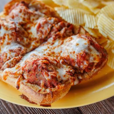 Chicken Parmigiana Sub with side of chips, close-up.