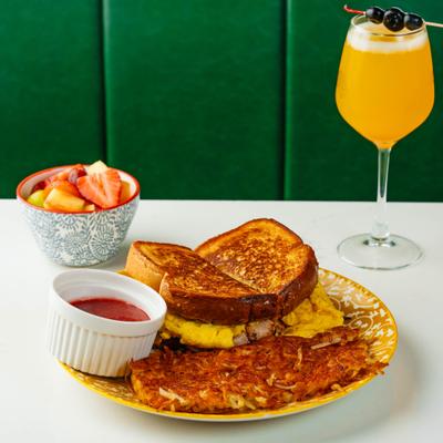 Breakfast French toast sandwich with eggs served with hash browns, mixed fruit, and a drink.