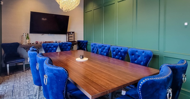 Big dining table with blue wing chairs, chandelier and the TV on the wall