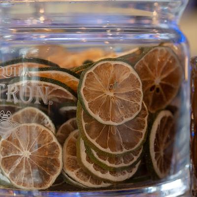 A close-up of dried lime slices stacked in a clear glass jar with Tequila and other text visible.