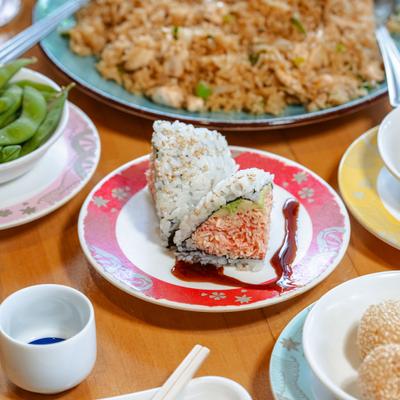 Stuffed rice triangle with sauce on patterned plate, surrounded by food plates.