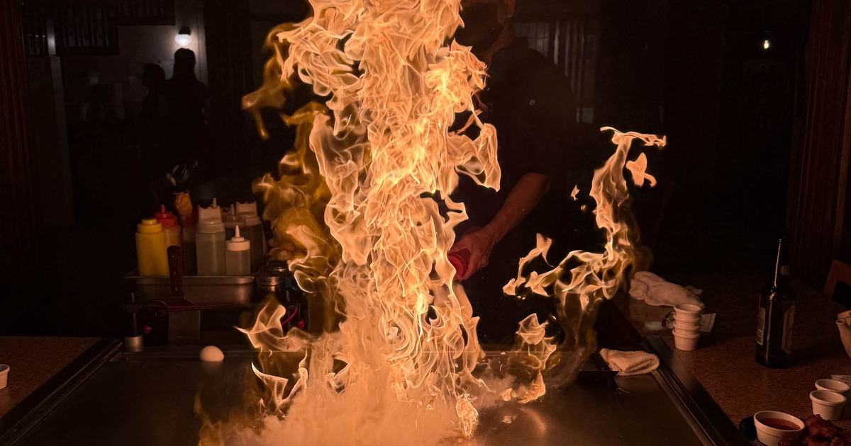 Chef performing a fire flambé technique on a flat-top grill