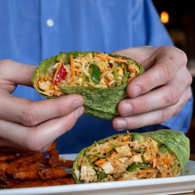 Hands holding a Spicy Thai Chicken Wrap.