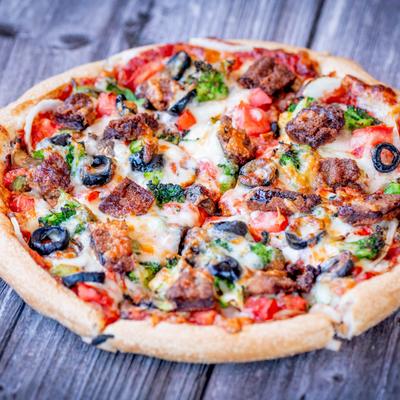 A veggie pizza sits on a weathered wooden table.