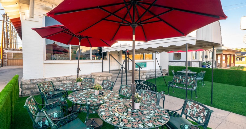 Outdoor patio with ornate tables, chairs, and red umbrellas on artificial turf
