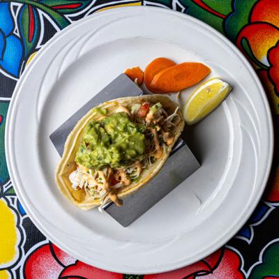 Overhead view of a shrimp taco topped with guacamole, served with a lemon wedge.