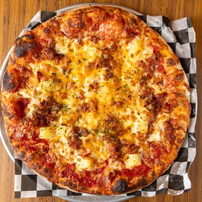 Hawaiian pizza with pineapple on a round tray.