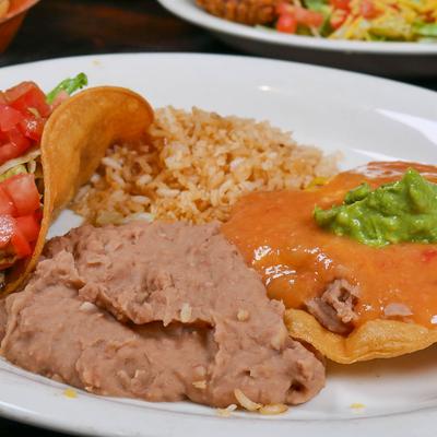 Mexican combination plate with taco, refried beans, rice, and enchilada topped with guacamole.