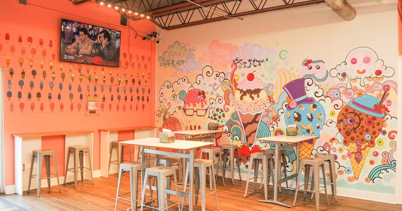 Interior, seating area with tables, bar stools, a TV, walls decorated with cartooned ice cream mural