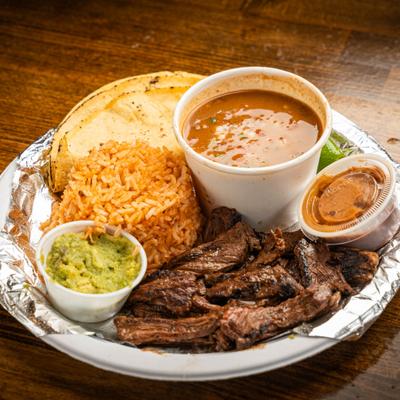 Carne asada served with rice, charro beans, guacamole, salsa, and soft tortillas.