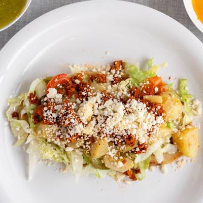 Tostada topped with lettuce tomatoes cheese and crema.