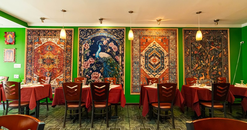 Restaurant interior, colorful, ornate tapestries, green wall, tables, red tablecloths, brown chairs