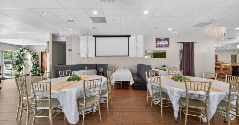Event space with tables, chairs, projector screen, and floral decorations