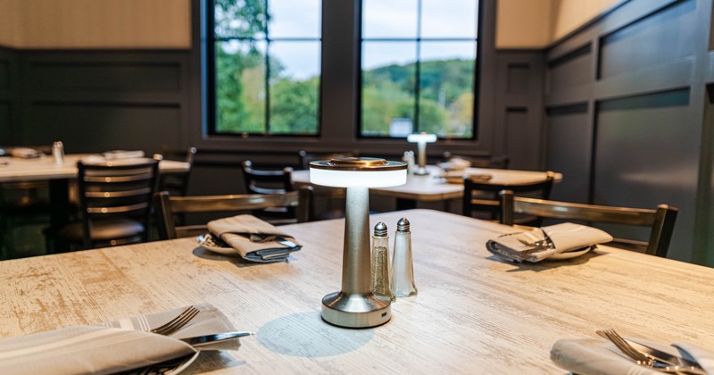 A restaurant interior featuring a wooden table set with a napkin, fork, plate, lamp