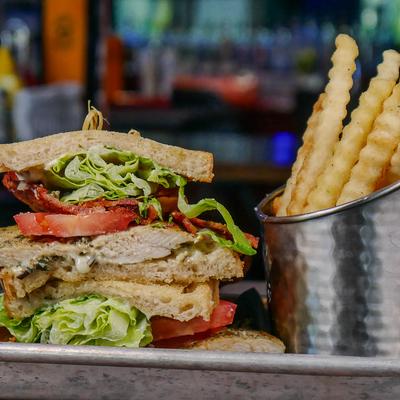 Chicken club sandwich with bacon, lettuce, and tomatoes, served with fries.