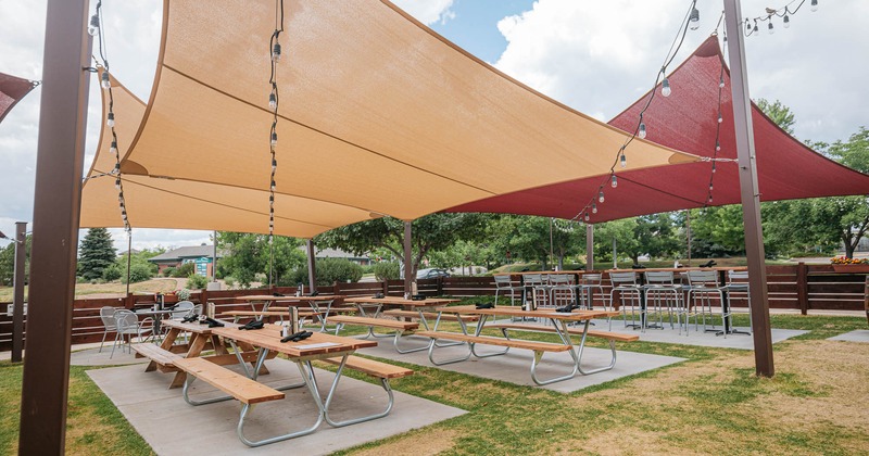 Patio area, long tables with bench seating and chairs, covered with shade sails