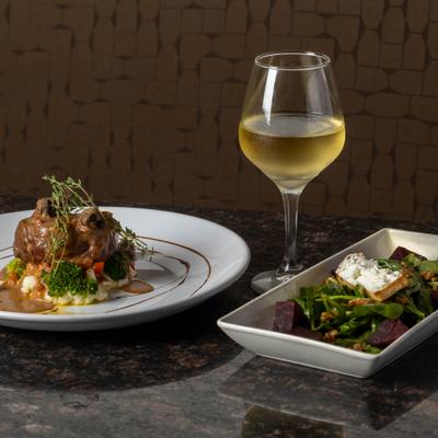 Plated gourmet meat dish served with white wine and salad.