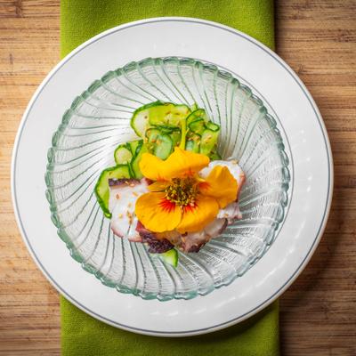 Sliced octopus paired with thinly sliced cucumber and garnish in a glass bowl.