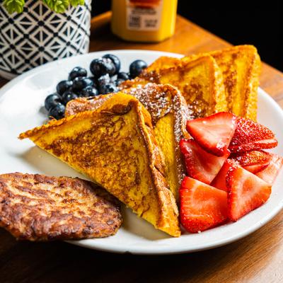 French toast with strawberries, blueberries, and a sausage patty on a white plate.
