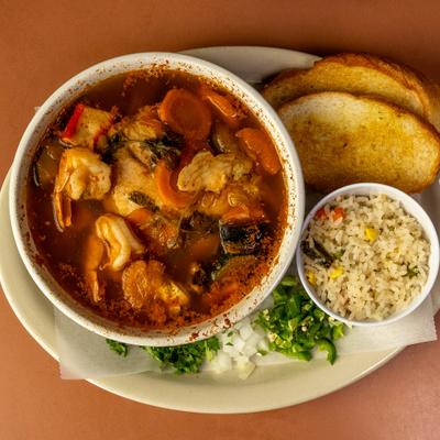 Bowl of seafood soup served with a side of rice and toasted bread.
