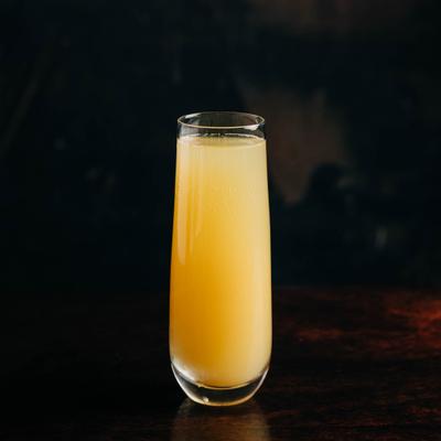 A glass of mimosa on a dark wooden table.