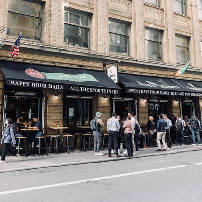 People gather outside Irish Times pub with a black awning.
