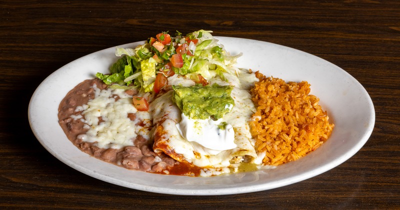 Enchiladas with green and red salsas, sour cream, guacamole, salad, rice, and beans