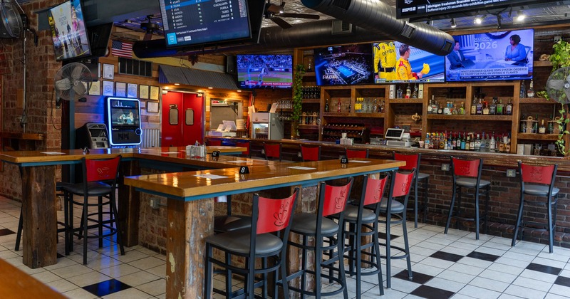 Sports bar interior with high top tables, bar seating, and multiple TVs