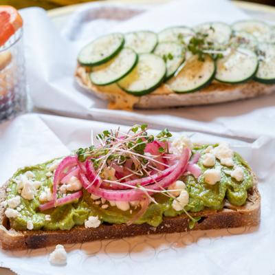 Avocado toast on sourdough topped with crumbled cheese, pickled red onions, and microgreens.
