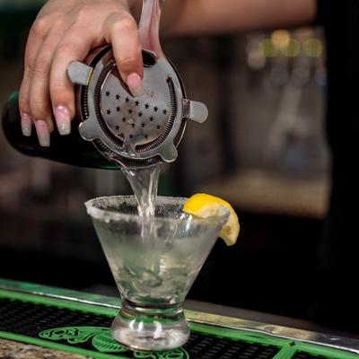 A bartender pouring lemon drop martini into a glass on bar mat, close up.