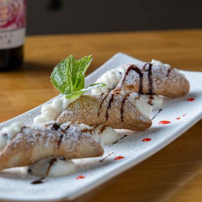 Cannoli with sweet cream filling, powdered sugar, chocolate drizzle, and mint garnish.