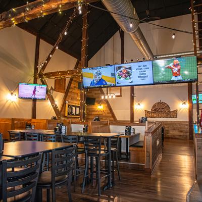 Restaurant dining area with both boot and table seating, string lights and several TV screens.