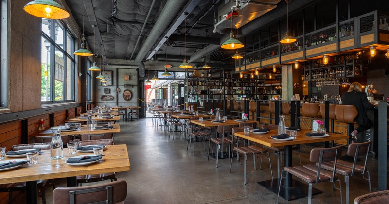Interior, dining area, wooden top tables for four, bar on the right, small lanterns