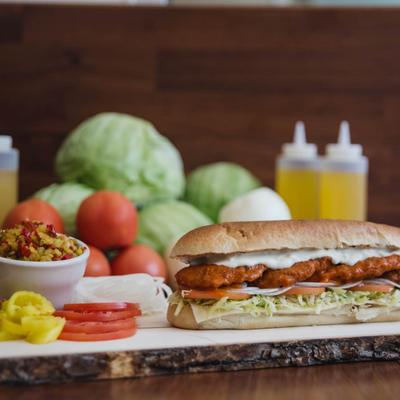 Chicken finger sub on a wooden board with a salad and slices of onion, tomato, banana peppers.