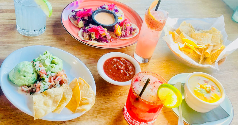Tacos, cheese dip, corn chips, chili and different cocktails on a table