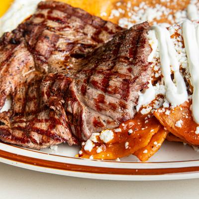 Chilaquilles served with grilled carne asada steak, close-up.