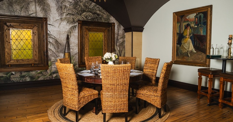 An elegant room with dining table and wicker chairs, palm-themed wallpaper and a large painting