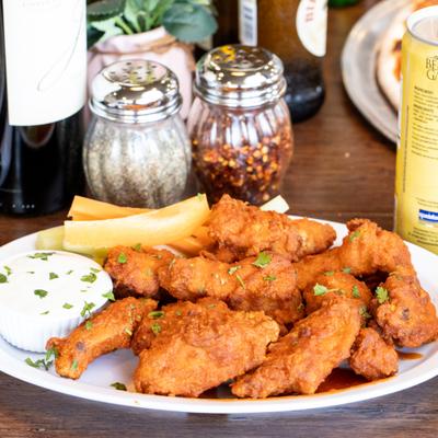 Buffalo chicken wings with celery sticks and blue cheese dip on a white plate.