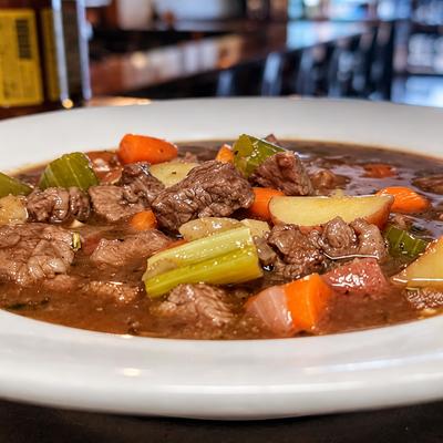 Beef stew with potato, carrot and celery in a white bowl on the pub counter..