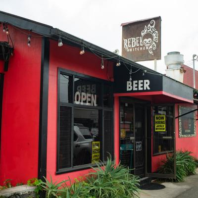 Restaurant exterior featuring a vibrant red facade, string lights and a hiring sign.