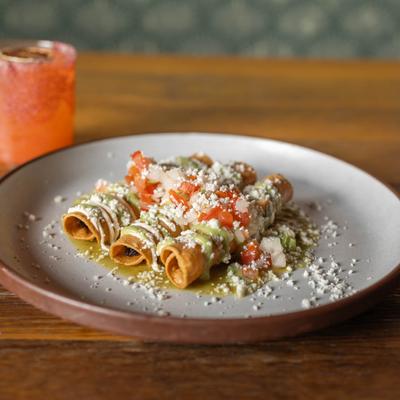 Chicken Taquitos, topped with cheese, Mexican cream, avocado sauce, and tomato.