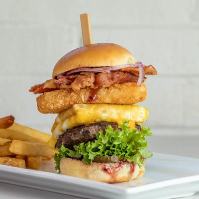 Burger with a fried egg, deep fried chicken, bacon, lettuce, onion, sauce, and fries.