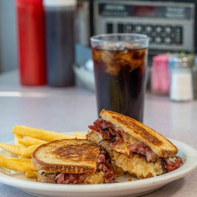 Reuben sandwich served with fries, alongside a drink.