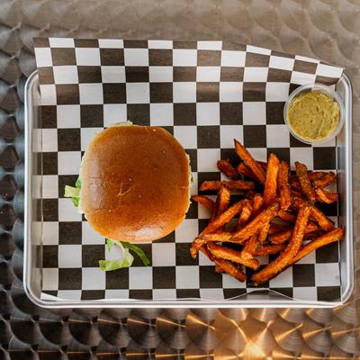 Burger with sweet potato fries and dip on a tray with checkered paper.