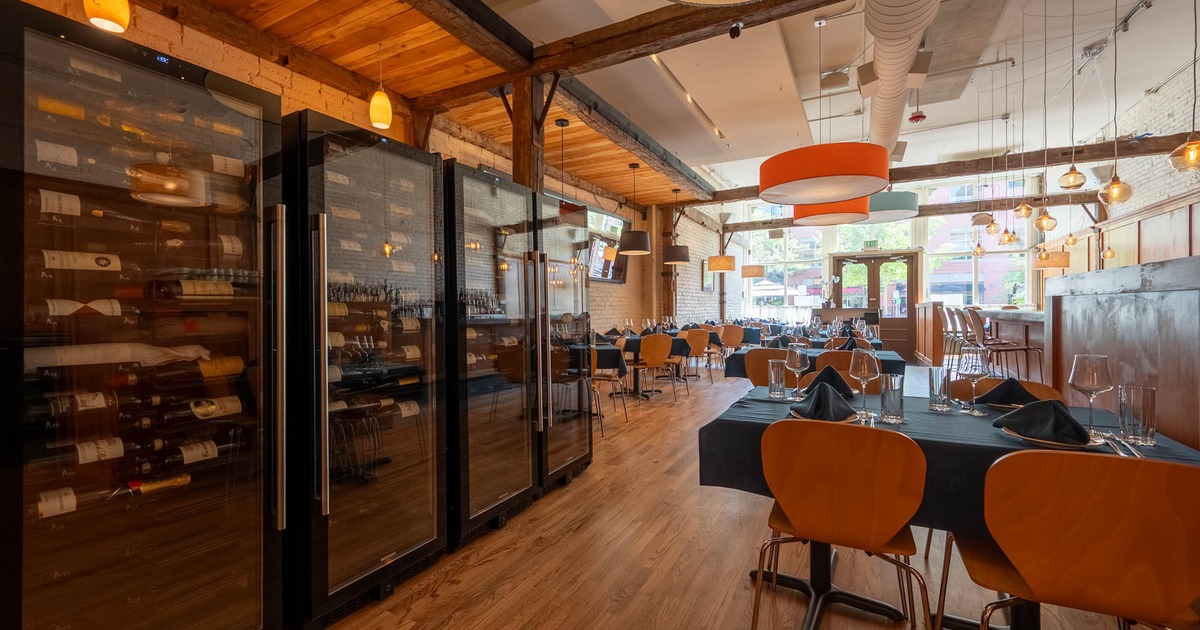 Rows of glass-door wine refrigerators stand in a restaurant with tables set for dining