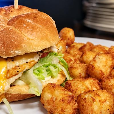 A chicken sandwich with lettuce served with golden tater tots..