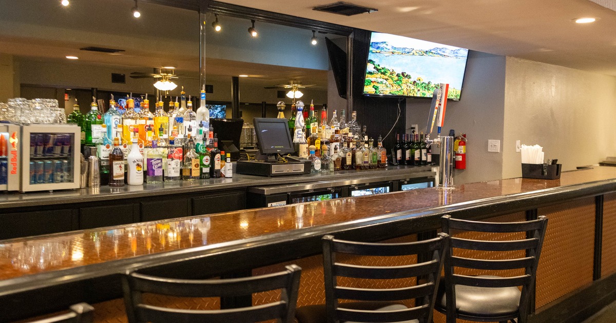 Stocked bar area with a wide variety of spirits, a counter and bar stools
