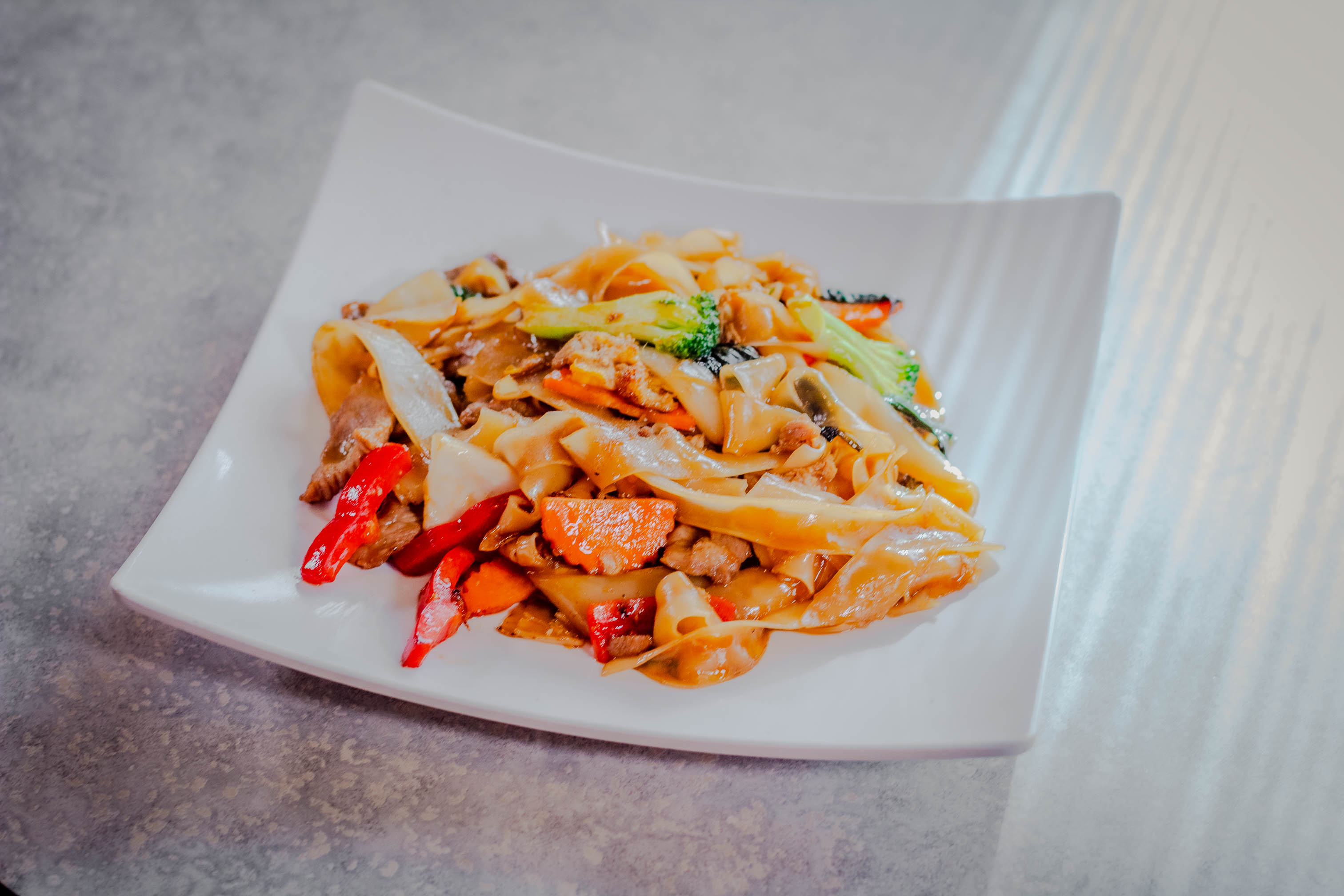 Plare of Drunken Noodles with carrot, broccoli, bell pepper, onion and basil