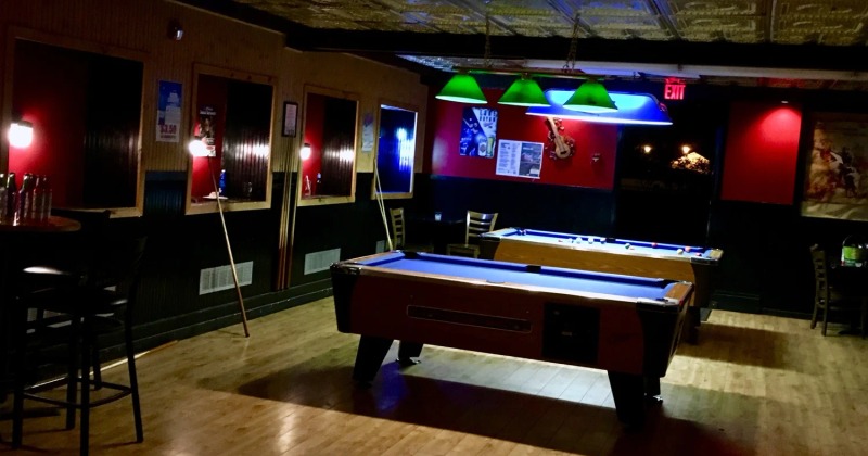 Interior featuring two pool tables illuminated by green pendant lights