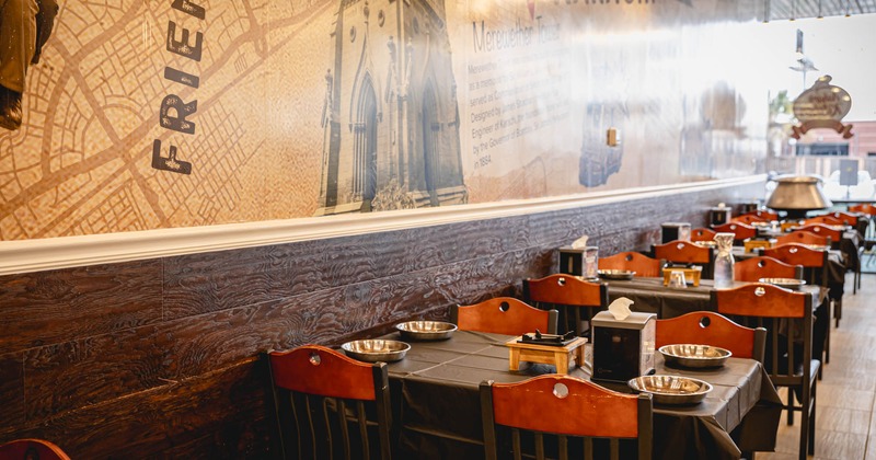 Interior, seating area, tables for four ready for guests, lower part of wall coated in wood